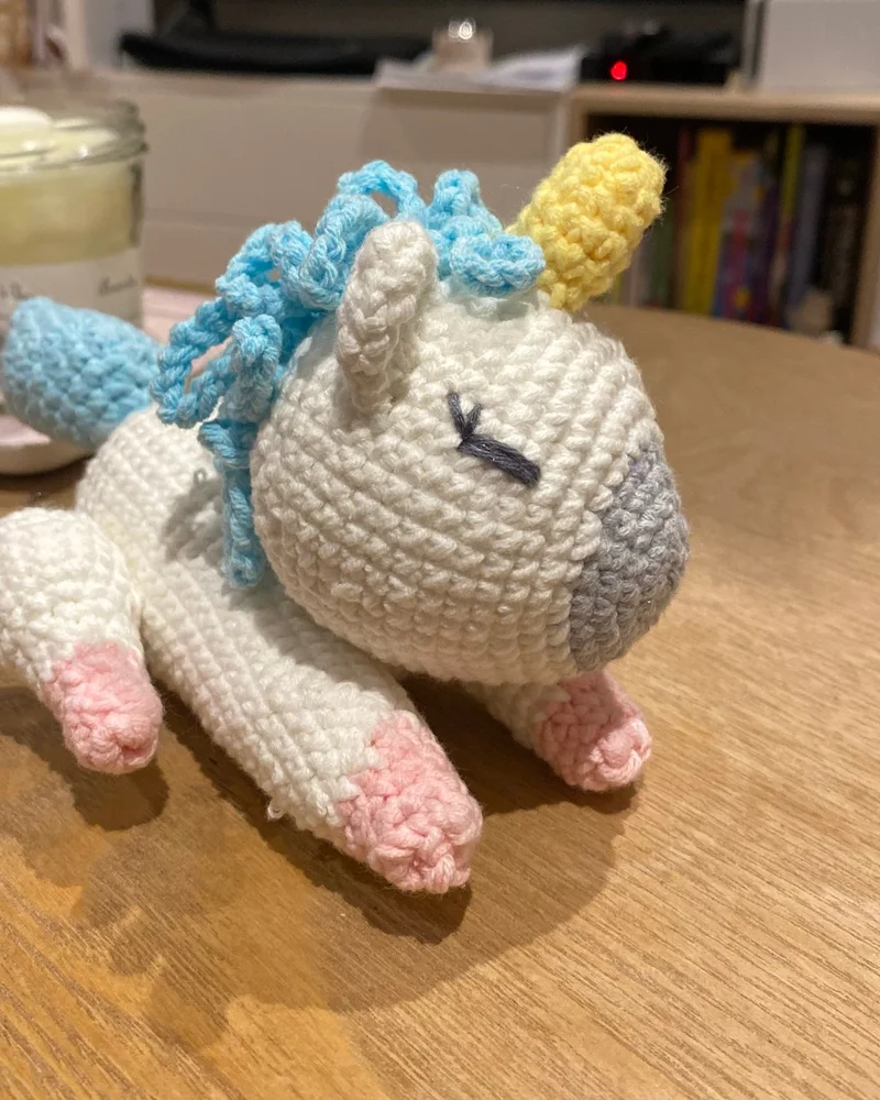 Licorne blanche crochetée à la main, crinière bleue et sabots roses.