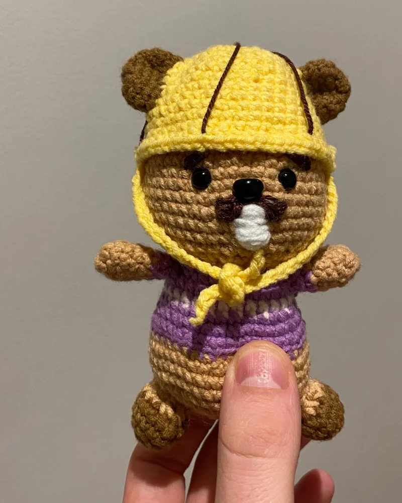 Petit personnage crocheté à la main, bonnet jaune et pull violet.