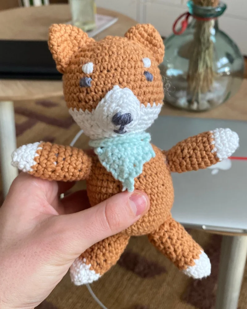 Renard orange et blanc crocheté à la main, avec une écharpe verte.